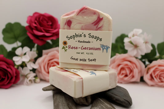 Two bars of Rose-Geranium goat milk soap with red and pink roses in the background
